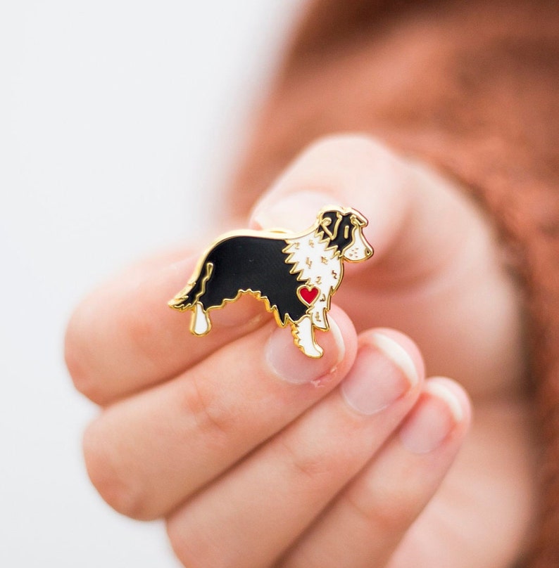 Border collie gold plated hard enamel pin badge. Black and white border collie design with a little red love heart on its chest held in a female hand.