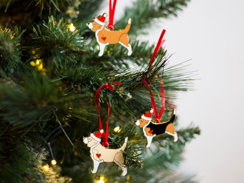 Puede incluir: Tres adornos navide&ntilde;os con forma de perros que llevan gorros de Pap&aacute; Noel. Los adornos est&aacute;n hechos de metal y tienen un acabado dorado. Los perros son de diferentes razas y colores, incluyendo un perro marr&oacute;n y blanco, un perro negro y blanco y un perro crema.