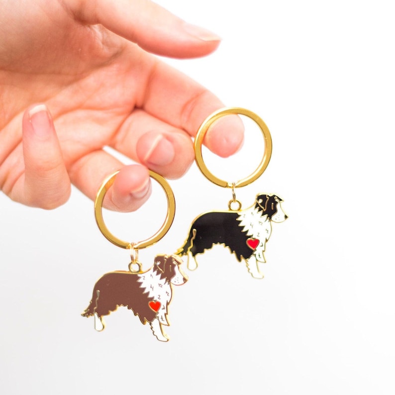 Border Collie dog enamel key-rings.  Coloured enamel with a little black nose, a red heart on the chest, gold plated lines and sand blasted on the reverse side. Dog keyring is attached to a gold plated split keyring hoop. Black and brown dog options.