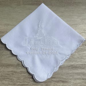 May include: A white square handkerchief with scalloped edges featuring white embroidery of a temple building. Below the building, the text reads Cody Temple and October 25 2026 in a white stitched font, centered on the fabric surface.