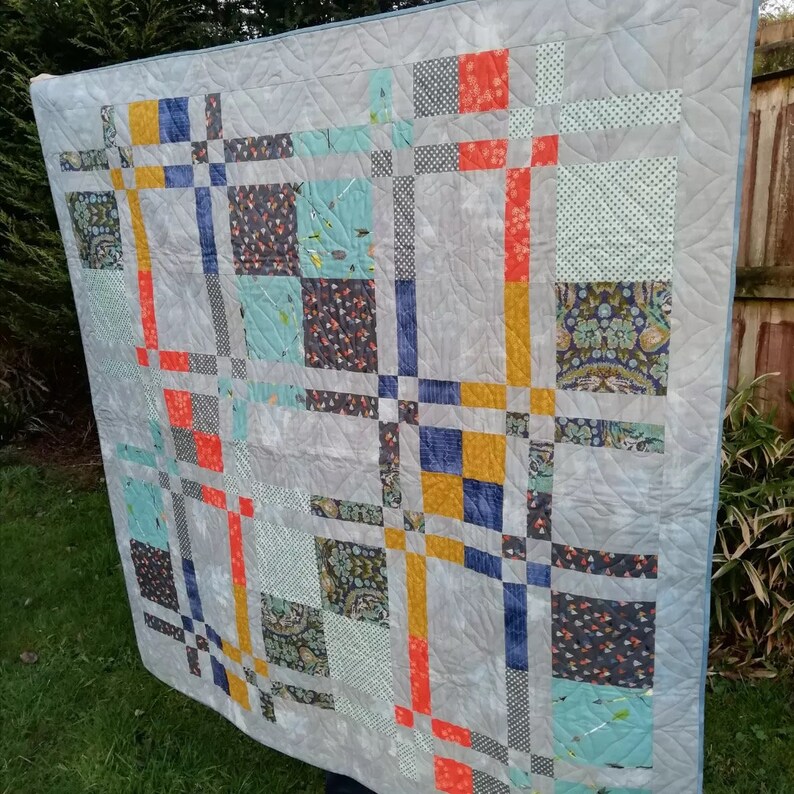 K&ouml;nnte beinhalten: Eine handgefertigte Steppdecke mit grauem Hintergrund und Patchwork-Design. Die Steppdecke zeigt Quadrate und Rechtecke in verschiedenen Farben, darunter Orange, Gelb, Blau und T&uuml;rkis. Die Steppdecke besteht aus Stoff mit verschiedenen Mustern.