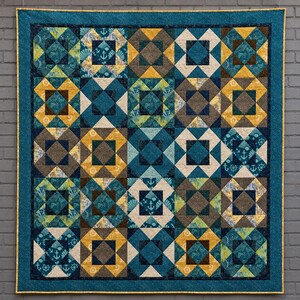 May include: A square quilt featuring a grid of alternating blocks in shades of teal, navy blue, mustard yellow, and brown. The design incorporates geometric patterns and nautical motifs, including anchors and ship wheels, finished with a teal border.