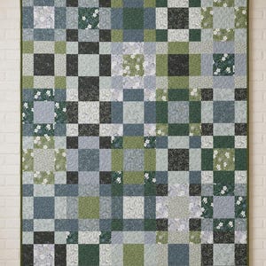 May include: A rectangular quilt featuring a patchwork grid pattern composed of various square fabric blocks in shades of sage green, forest green, slate blue, and light grey, with some blocks displaying small white floral and botanical prints.