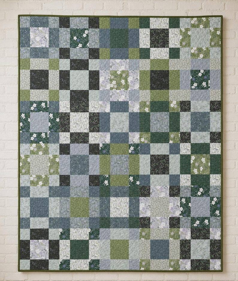 May include: A rectangular quilt featuring a patchwork grid pattern composed of various square fabric blocks in shades of sage green, forest green, slate blue, and light grey, with some blocks displaying small white floral and botanical prints.