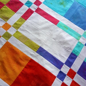 K&ouml;nnte beinhalten: Ein farbenfroher Quilt mit einem geometrischen Muster. Das Design zeigt Quadrate und Rechtecke in Rot-, Orange-, Gr&uuml;n-, Blau- und Lilat&ouml;nen, getrennt durch wei&szlig;e Streifen. Der Quilt hat eine strukturierte Oberfl&auml;che.