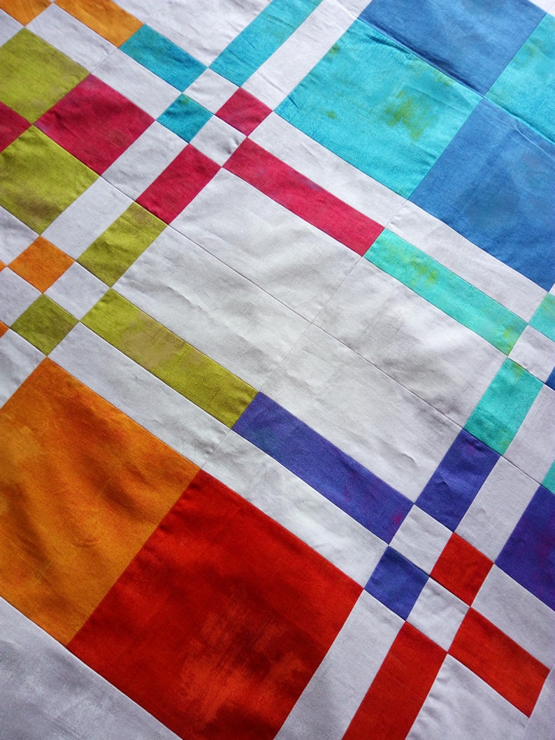 K&ouml;nnte beinhalten: Ein farbenfroher Quilt mit einem geometrischen Muster. Das Design zeigt Quadrate und Rechtecke in Rot-, Orange-, Gr&uuml;n-, Blau- und Lilat&ouml;nen, getrennt durch wei&szlig;e Streifen. Der Quilt hat eine strukturierte Oberfl&auml;che.