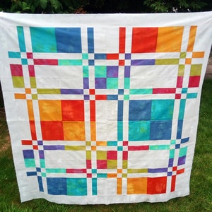 K&ouml;nnte beinhalten: Ein farbenfrohes Quilt mit wei&szlig;em Hintergrund und einem Rastermuster aus Quadraten und Rechtecken in Blau-, Orange-, Rot-, Gr&uuml;n- und Lilat&ouml;nen. Das Quilt h&auml;ngt im Freien.