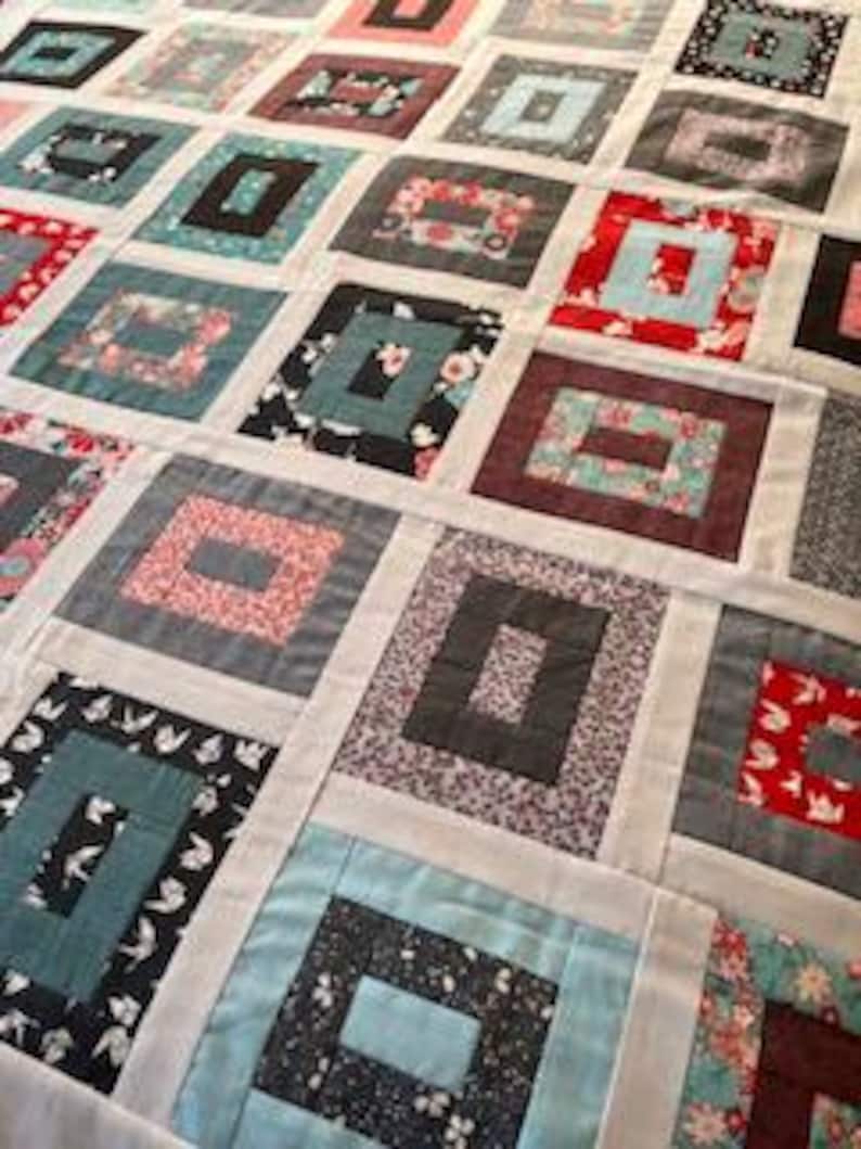 May include: A patchwork quilt featuring a repeating log cabin block pattern. The quilt is composed of various fabric squares in shades of red, blue, black, grey, and white, with floral, bird, and geometric prints separated by white sashing strips.