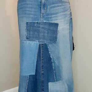 May include: A long denim skirt made from patchwork denim fabric. The skirt has a straight silhouette and a frayed hem.