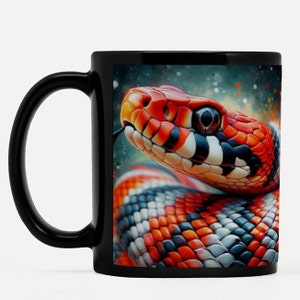 May include: Black ceramic mug with a detailed illustration of a snake's head. The snake has a red and orange head, with black and white markings on its body. The mug's handle is black.