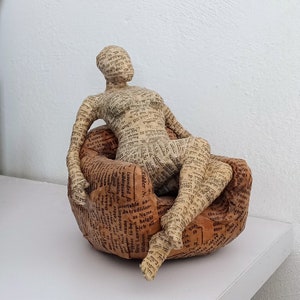 Donna che legge seduta su una sedia comoda, scultura di cartapesta,