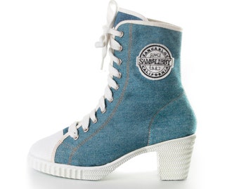 May include: Blue denim high-heeled boots with white laces and a white sole. The boots have a round toe and a white patch on the side that says "San Carlos Since 1987 Sam's Libby California".