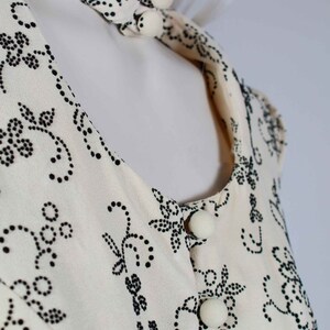 May include: A white blouse with a black floral pattern and white buttons. The blouse has a round neckline and short sleeves.