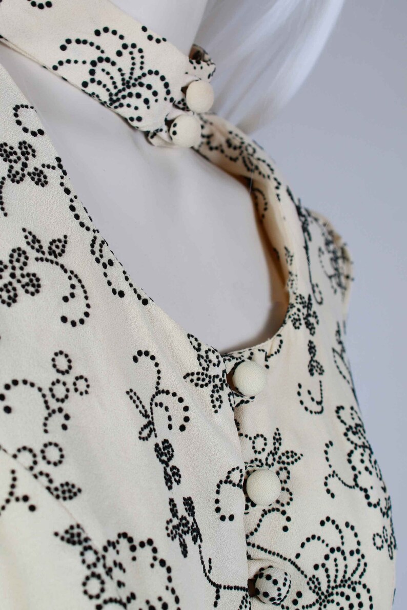 May include: A white blouse with a black floral pattern and white buttons. The blouse has a round neckline and short sleeves.