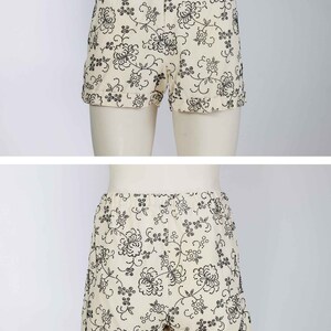 May include: White shorts with a black floral pattern. The shorts have a cuffed hem and a waistband with a button and zipper closure.