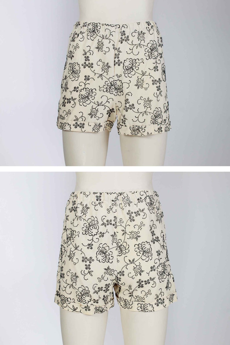 May include: White shorts with a black floral pattern. The shorts have a cuffed hem and a waistband with a button and zipper closure.