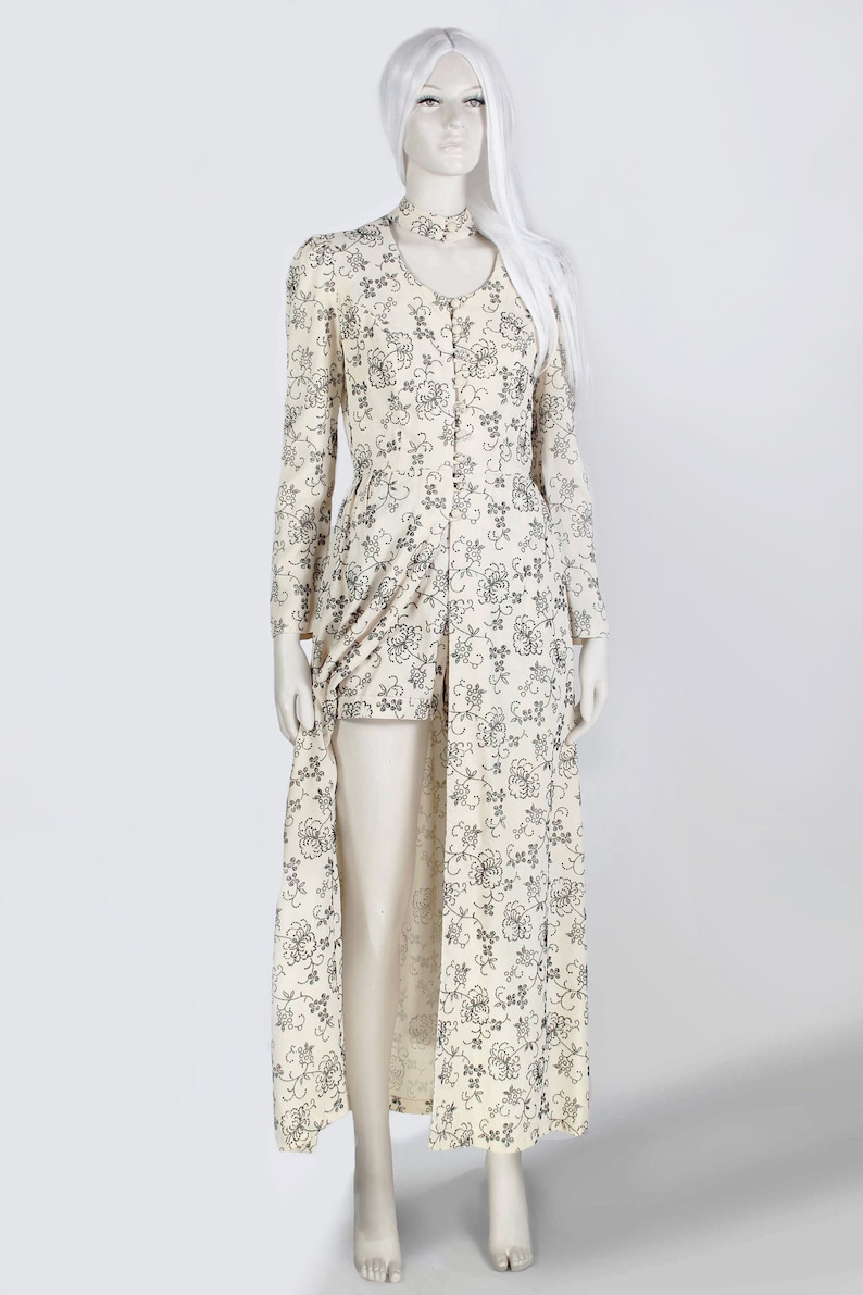May include: A long white dress with a floral pattern. The dress has a high neckline and long sleeves. The dress is made of a lightweight fabric and has a flowing silhouette.