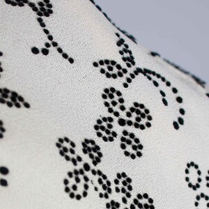 May include: White fabric with a black floral pattern. The pattern is made of small black dots that form flowers.