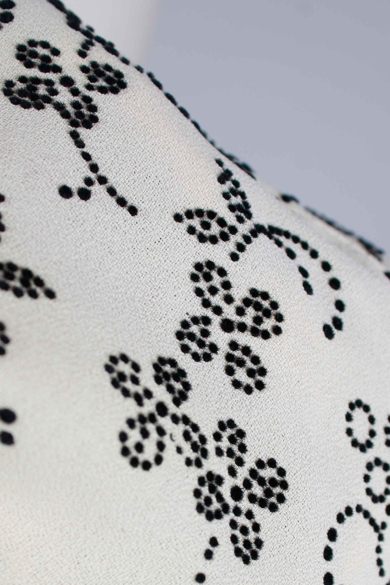 May include: White fabric with a black floral pattern. The pattern is made of small black dots that form flowers.