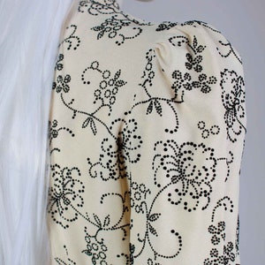 May include: A cream-colored blouse with a black floral pattern. The pattern is made up of small black dots that form flowers and vines.