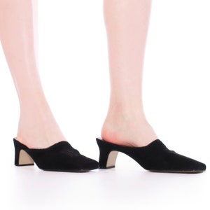 May include: A pair of black suede heeled mules with a low block heel. The shoes have a closed toe and a slip-on design.