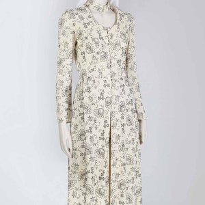 May include: A long white dress with a black floral pattern. The dress has a high neckline and long sleeves. It is a vintage style dress.
