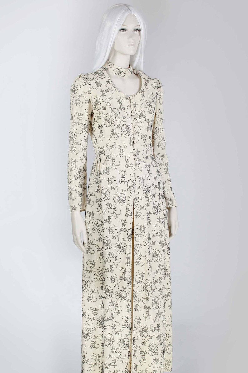 May include: A long white dress with a black floral pattern. The dress has a high neckline and long sleeves. It is a vintage style dress.