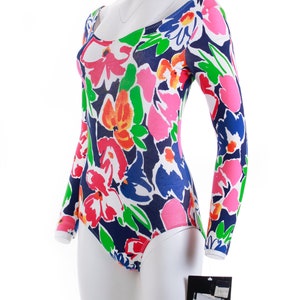 May include: A long-sleeved bodysuit with a floral print in shades of pink, red, orange, green, white, and blue. The bodysuit has a scoop neck and a fitted silhouette.