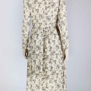 May include: A long, white dress with a black floral pattern. The dress has a high neck and long sleeves.