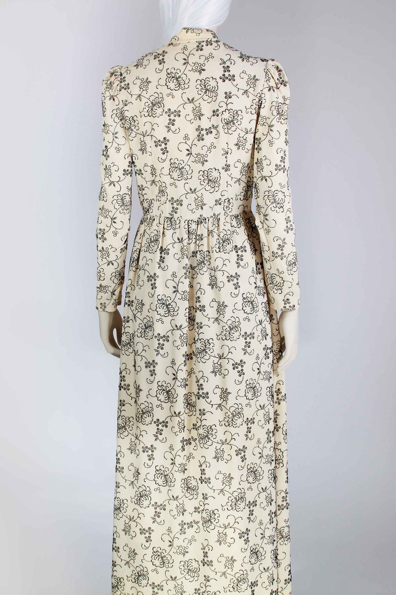 May include: A long, white dress with a black floral pattern. The dress has a high neck and long sleeves.