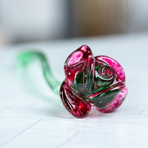 May include: A handcrafted glass rose sculpture with a vibrant color palette. The rose features deep red and green hues, with a delicate green stem. The glasswork is detailed, showcasing the petals' intricate design. This decorative piece is ideal for home decor.