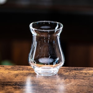 May include: A clear glass whisky tasting glass with a wide base and a narrow top. The glass is sitting on a wooden surface.