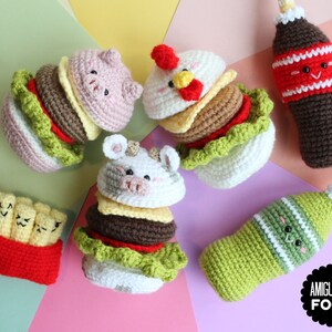 May include: A collection of crocheted amigurumi food items including three animal-themed burgers, a red container of fries with faces, and two beverage bottles with faces. The text AMIGURUMI FOOD is printed in white on a black scalloped circular badge.