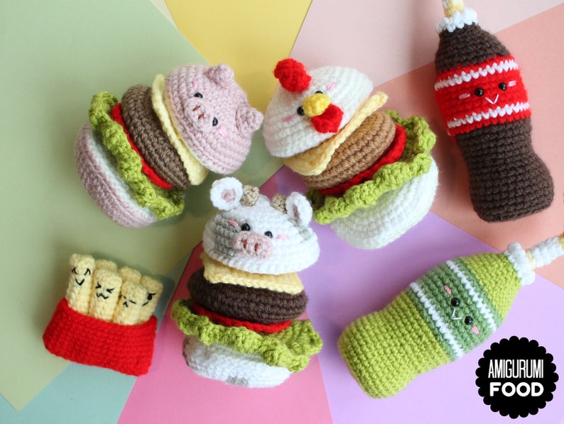 May include: A collection of crocheted amigurumi food items including three animal-themed burgers, a container of french fries, and two beverage bottles. Each item features embroidered facial expressions. A black logo reads AMIGURUMI FOOD.