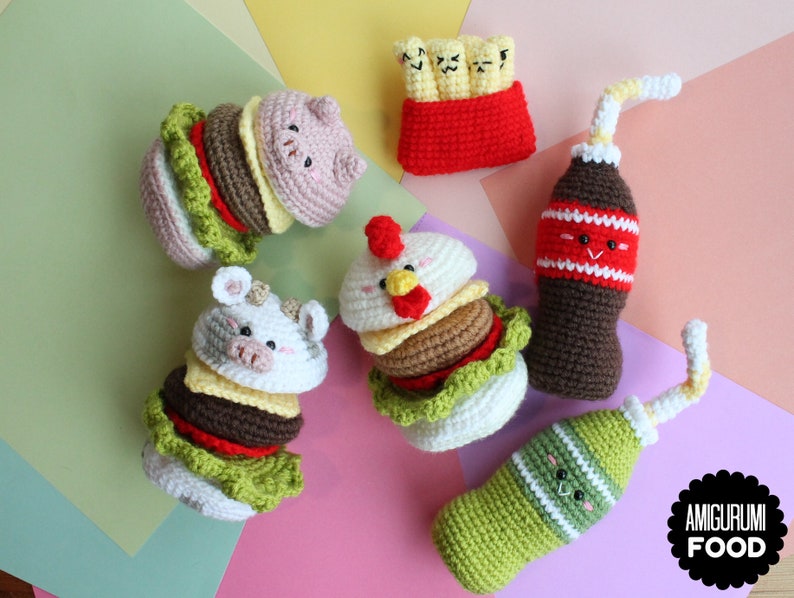 May include: A collection of crocheted food items including two animal-themed burgers, a container of fries with faces, and two bottles with straws and faces. The items feature various colors like brown, green, red, white, and yellow. Text reads AMIGURUMI FOOD.