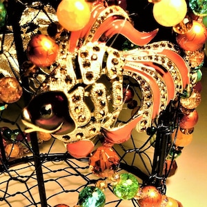 May include: A black wire cage with a gold and red jeweled fish ornament. The cage is decorated with colorful beads in shades of green, red, orange, and gold.