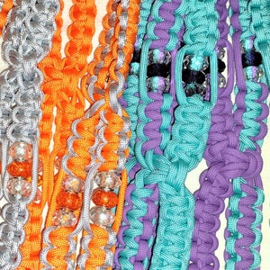 Op de afbeelding: Drie strengen gevlochten koord, een oranje en zilver, een teal en paars, en een paars. Elke streng heeft kralen die in de vlecht zijn geweven.