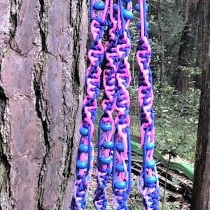 May include: A close-up of a pink and blue braided rope with blue beads hanging from a tree. The rope is tied to a branch and is hanging down.