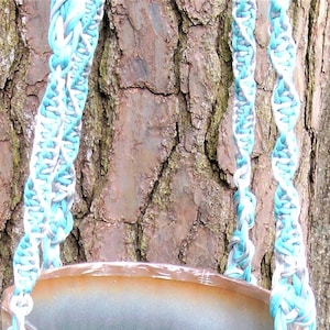 May include: Two macrame plant hangers made with white, gray, and light blue cord. The hangers are hanging from a tree trunk.