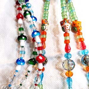 May include: Multi-strand beaded necklace with colorful glass beads, including clear crystal beads, red, orange, green, and blue beads, and white and colorful mushroom-shaped beads. The necklace also features small owl-shaped beads with painted details.