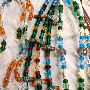 May include: Three strands of beaded necklaces with green, blue, and orange beads. Each strand features small ceramic fish and turtle charms.