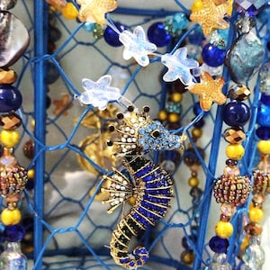 May include: A blue wire cage decorated with blue, gold, and clear beads, starfish, and a jeweled seahorse.
