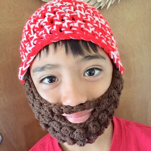 May include: A child wearing a red and white crocheted hat with a brown crocheted beard attached.