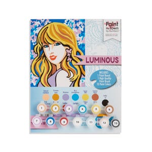 May include: A paint-by-numbers kit titled "Luminous" featuring a pop art style illustration of a woman with blonde hair. The kit includes a paint board, brush, and 13 paint colors. The kit is made in Nashville, USA.