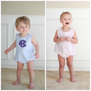 Pode incluir: Dois bebês usando macacões listrados combinando. O macacão à esquerda é azul e branco com um monograma roxo "ABC". O macacão à direita é rosa e branco.