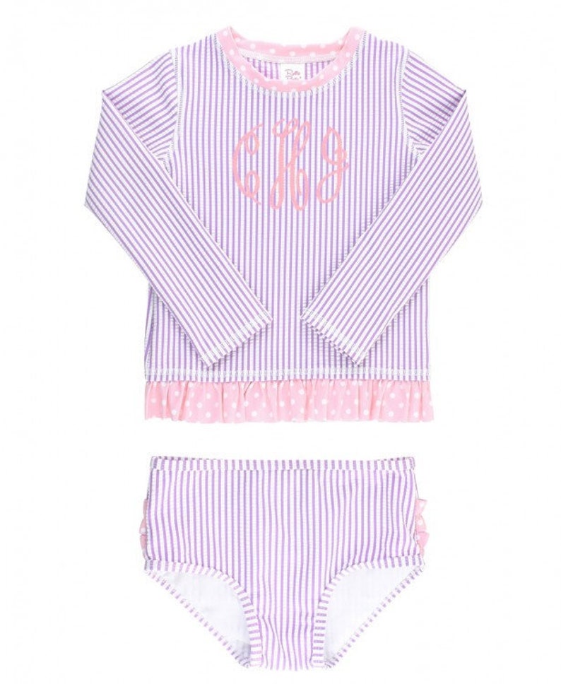 May include: A purple and white striped swimsuit with pink polka dot trim and a ruffle detail. The top has long sleeves and a monogrammed "CJS" on the front.