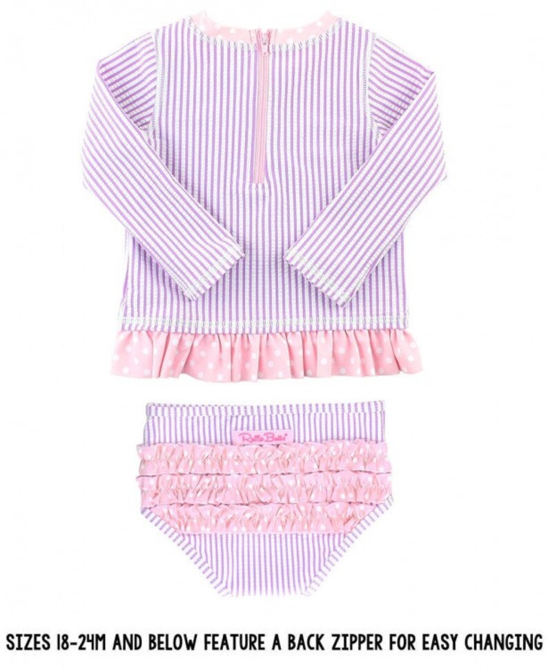 May include: A purple and white striped long-sleeved swimsuit with a pink polka dot ruffle trim. The swimsuit has a back zipper for easy changing. The matching bottoms are also purple and white striped with a pink ruffle trim.