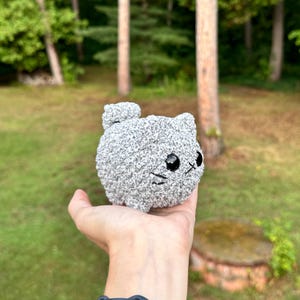 K&ouml;nnte beinhalten: Ein kleines, graues, flauschiges, geh&auml;keltes Katzenspielzeug mit schwarzen Augen und einem wei&szlig;en gestickten Mund.
