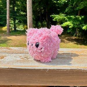 K&ouml;nnte beinhalten: Ein rosa flauschiges Pl&uuml;schtier mit schwarzen Augen und einem kleinen Schwanz. Das Spielzeug sitzt auf einer Holzoberfl&auml;che.