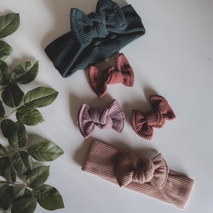 May include: Four fabric headbands with knotted bows. Two headbands are a dark teal color, one is a light pink, and one is a dark pink.